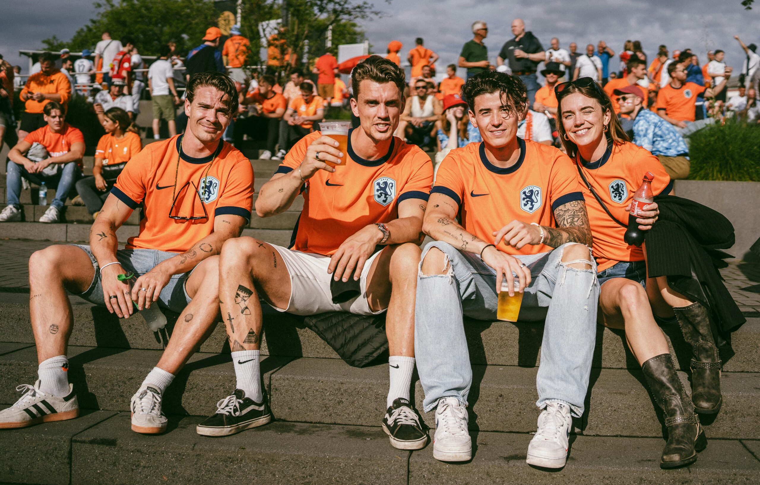 Group of young adults in orange soccer jerseys enjoying a day at a sports event outdoors.