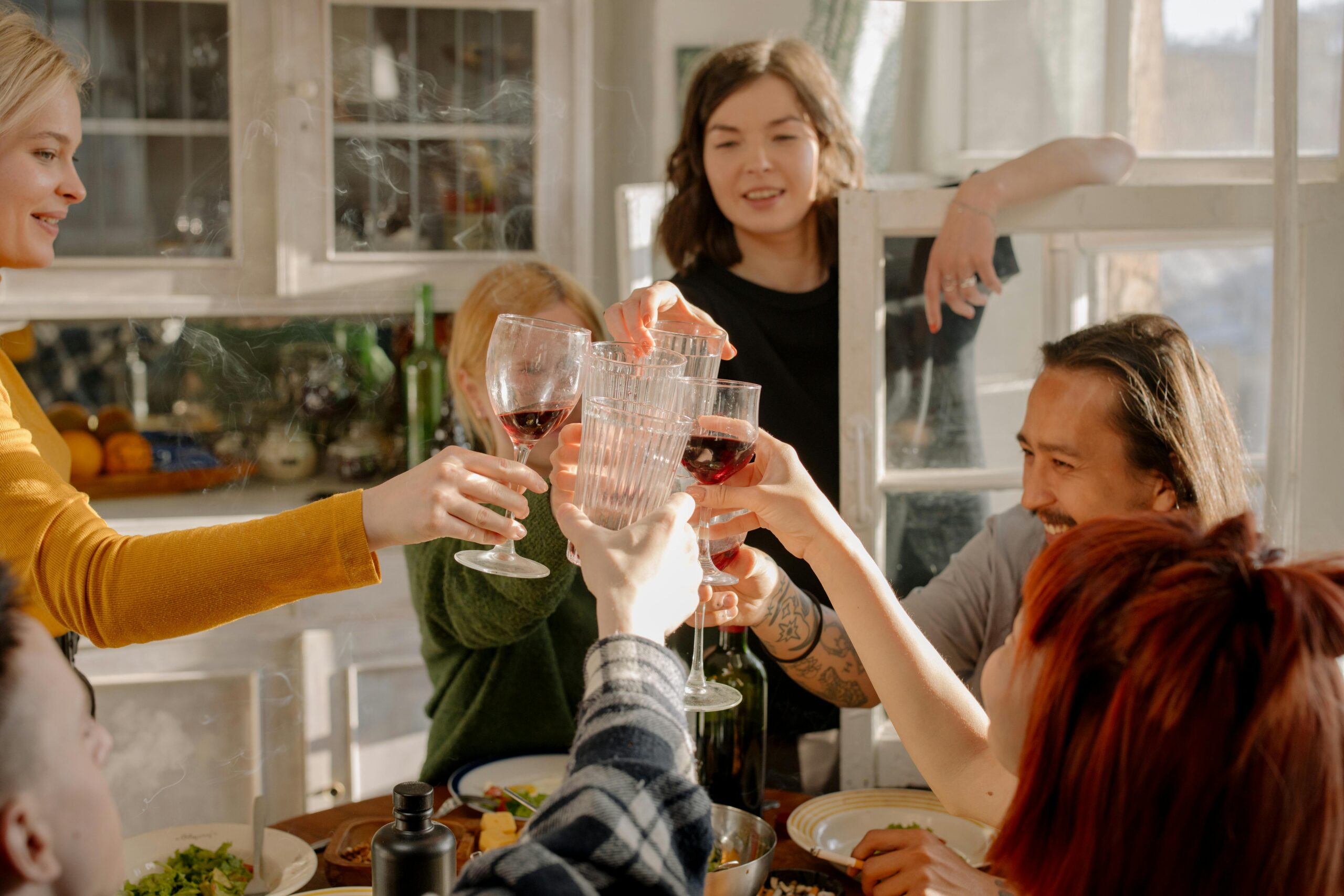 A group of friends celebrates and cheers with wine glasses in a cozy kitchen setting.