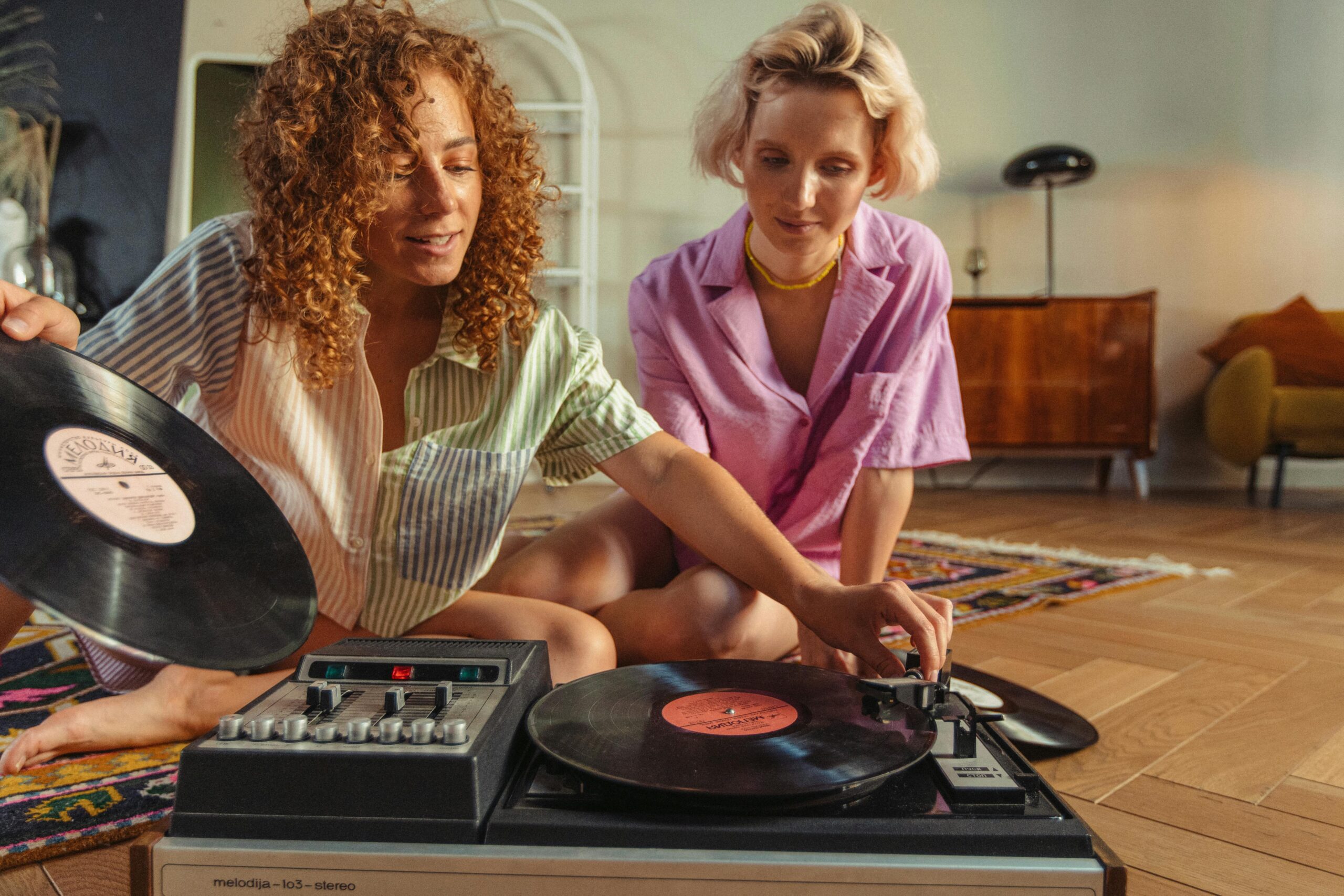 Two women enjoying music on a vintage turntable, sharing a close and relaxing moment indoors.